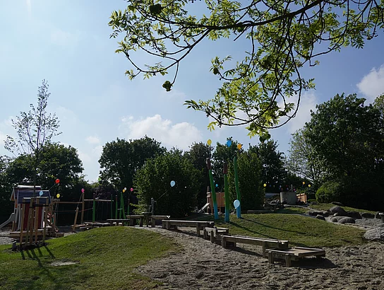 Blick auf einen Spielplatz mit Wasserrinne, die zu einem Sandkasten führt.