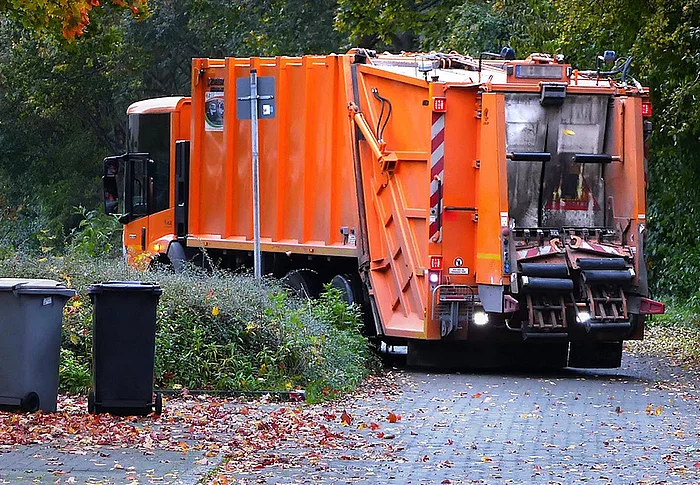 Orangefarbenes Müllfahrzeug fährt um eine Kurve.