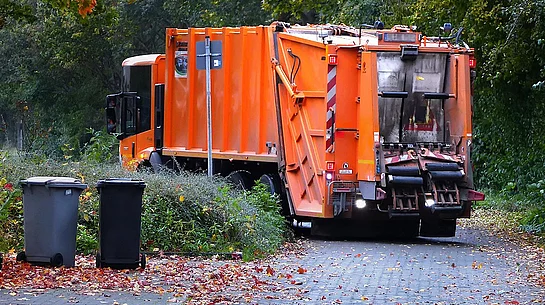 Orangefarbenes Müllfahrzeug fährt um eine Kurve.