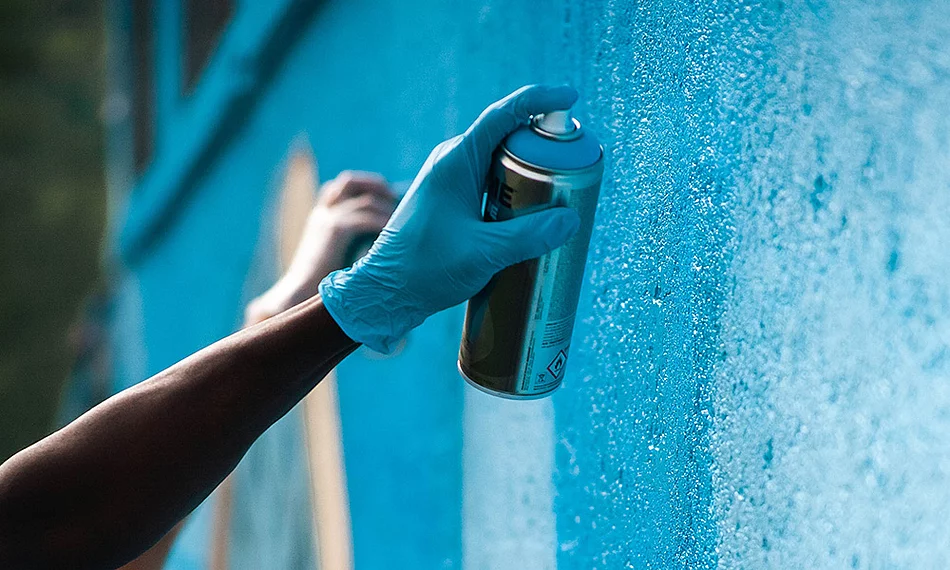 Eine Hand hält eine Sprühdose und sprayt ein Graffiti an eine Wand.