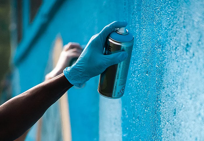 Eine Hand hält eine Sprühdose und sprayt ein Graffiti an eine Wand.