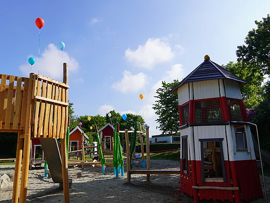 Spielplatz mit einem Podest aus Holz und einem Spielhaus in Form eines Leuchtturms. 